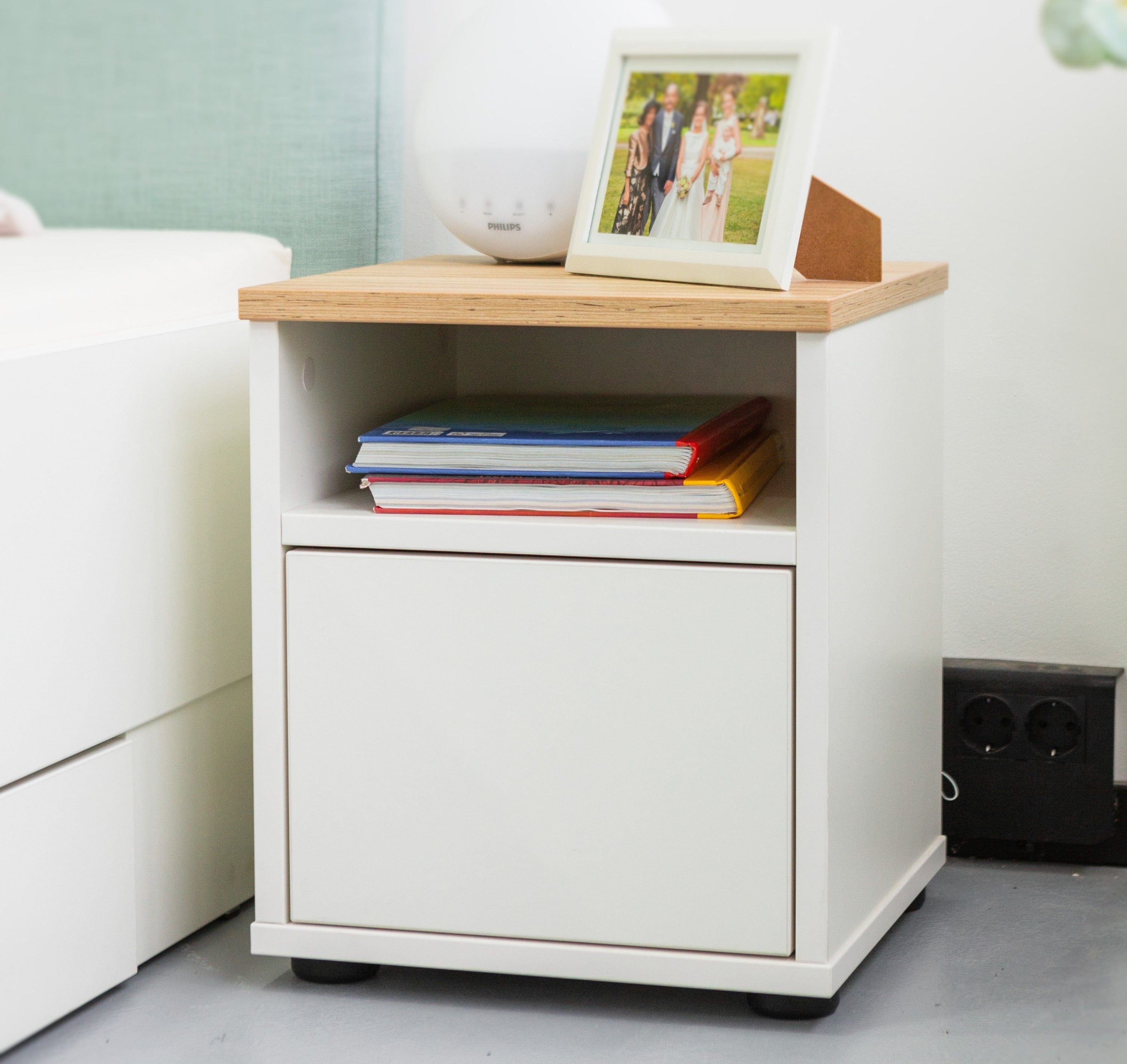 Seitlicher Blick auf den Liegewiese Nachtschrank in Weiß Coco Bolo mit Dekoration in modernem Schlafzimmer